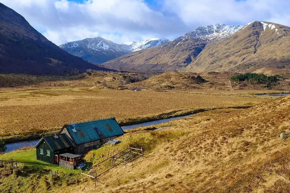 Rustic building by a stream in a valley with snow-capped mountains