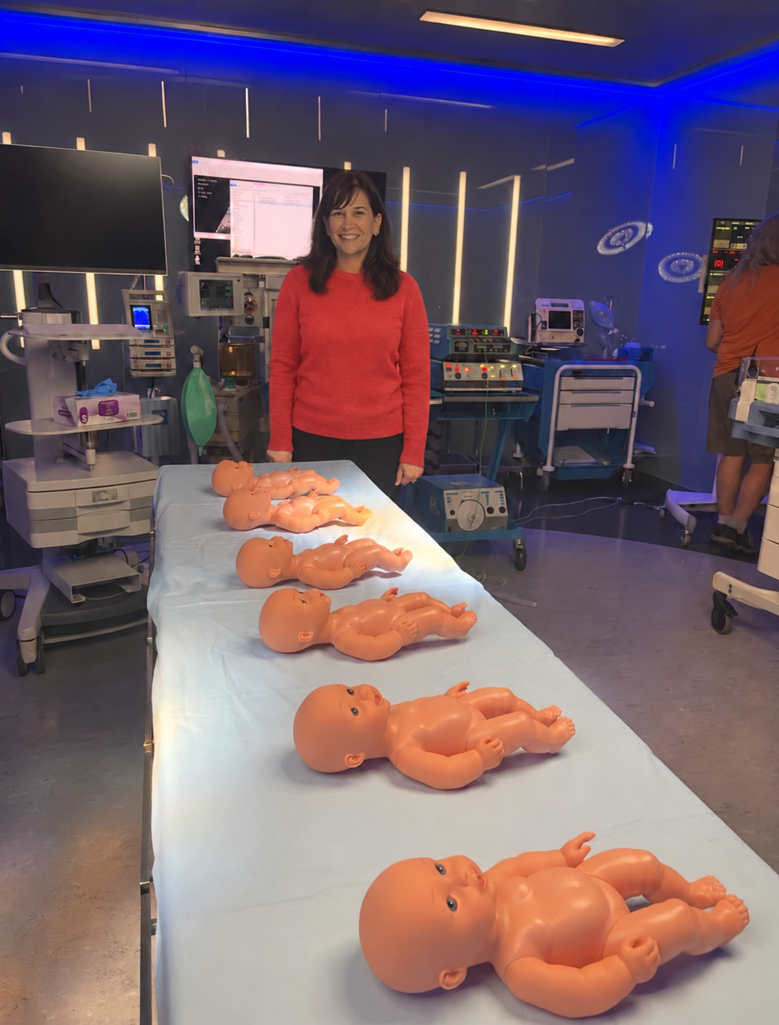Dr. Brandy beside infant mannequins and medical equipment on a set.