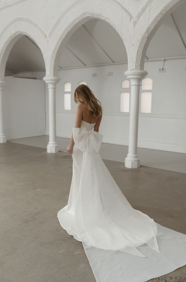 Madi Lane Silas bridal gown wedding dress stretch satin pleated bodice strapless v neck fit and flare detachable bow train 