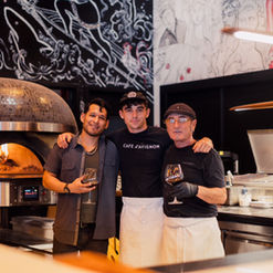 Three Pizza Lab employees standing by pizza oven