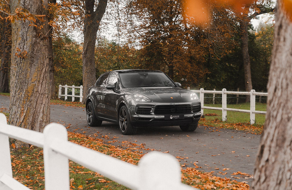 Un porsche Cayenne Coupé, SUV gris sur route de campagne avec feuille d'automne, entouré d'arbres et clôture blanche. Atmosphère paisible et automnale.