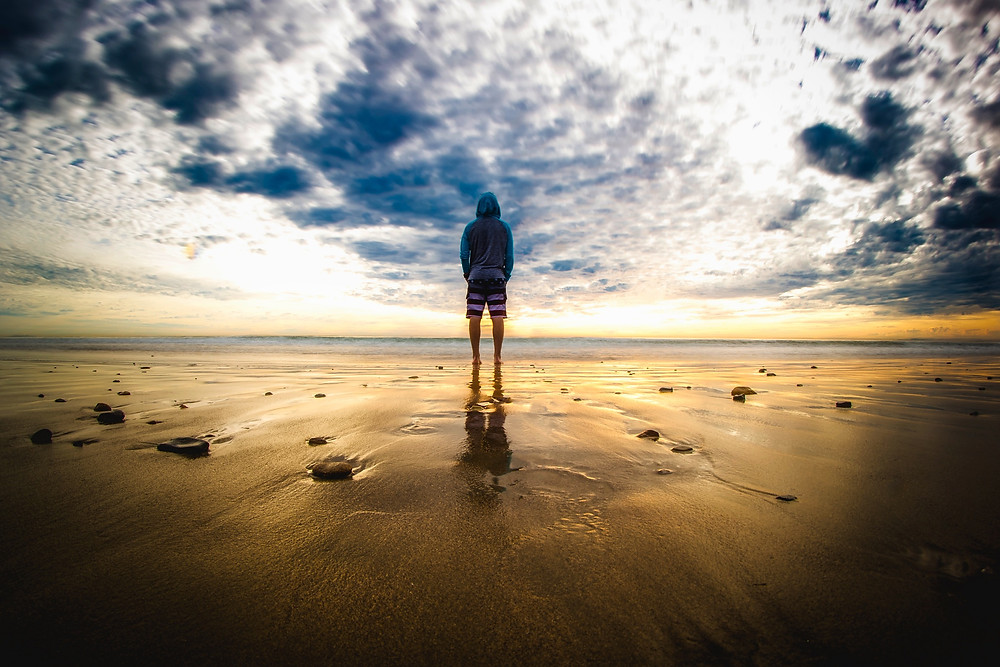 Man standing looking at sea, sunset, sunrise, beach