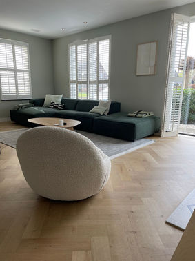 Een foto van de woonkamer met een groene bank, een witte draaistoel met boucle stof en een visgraat vloer