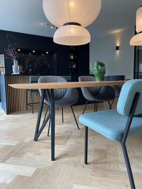 Een foto van de eettafel met op de achtergrond de zwarte keuken. De lampen staan aan.