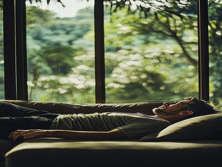 An American male professional wearing jeans and a t-shirt, taking a nap in his Singaporian house with green trees in his backyard