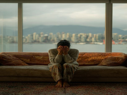 An Indian woman sitting on her orange couch in her west vancouver home with her hands on her face because she is depressed