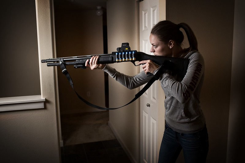 A homeowner holding a home defense shotgun inside a house, demonstrating a common firearm option for home protection.