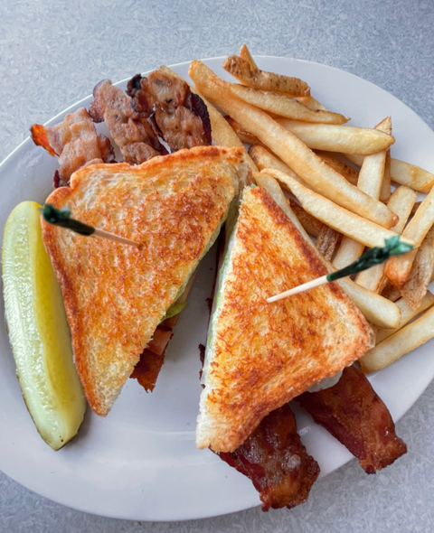 Bacon, lettuce and tomato sandwich with french fries and a pickle on the side