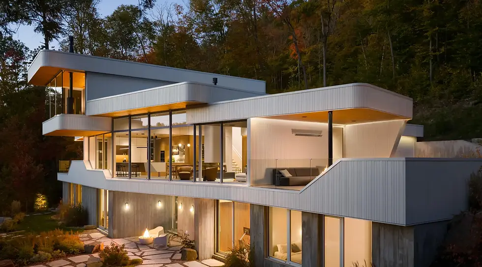 The Albatross: a Modern Marvel in the Laurentians
Modern house with large glass windows, glowing warmly at dusk. Surrounded by trees and a stone path, evoking a peaceful ambiance.