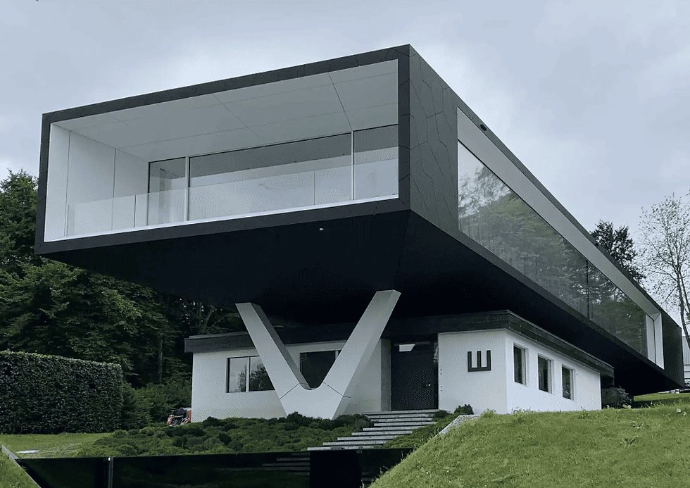 Modern cantilevered house with glass walls and white exterior, set in a lush green landscape. Overcast sky enhances its sleek design.