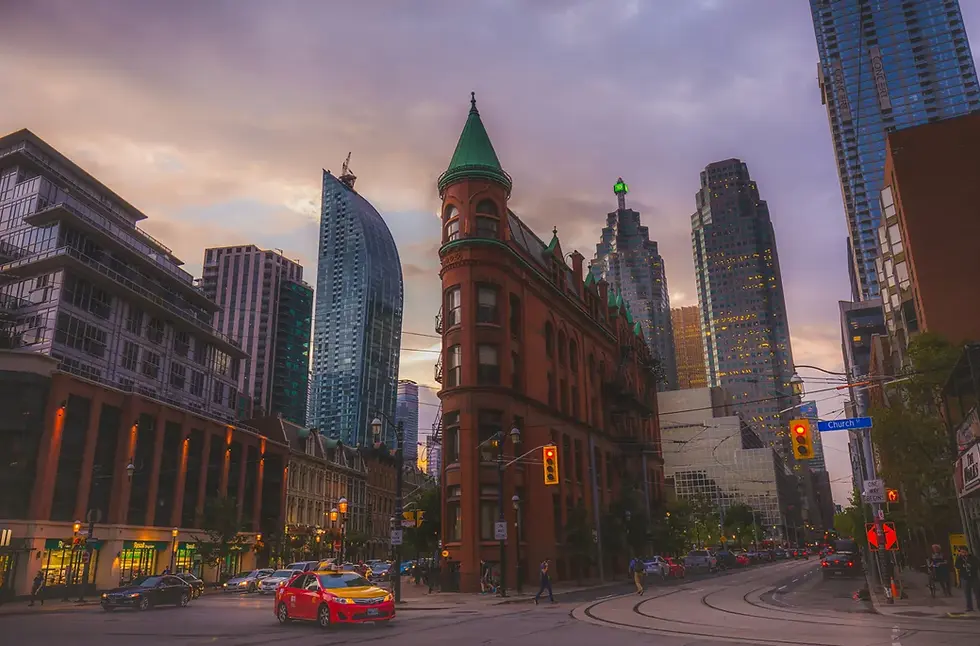 City street at dusk with red brick flatiron building, modern skyscrapers, cars, and streetlights. Moody sky, "Church St" sign visible.
