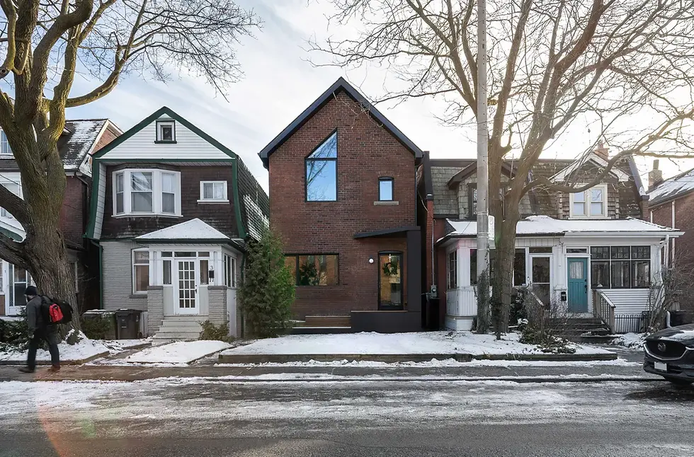 Snowy street with brick houses and trees. A person with a red backpack walks by. The scene is serene and wintry.