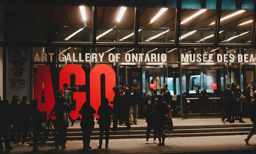 People gather at the entrance of the Art Gallery of Ontario at night, with bright red "AGO" letters and glass facade, creating a lively mood.