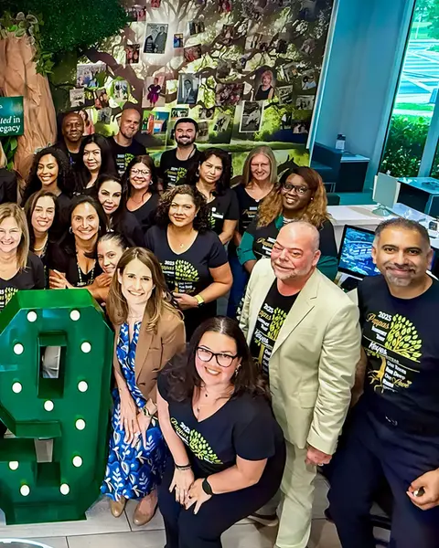 Smiling team members pose together in front of a tree wall filled with family photos and legacy roots decor.