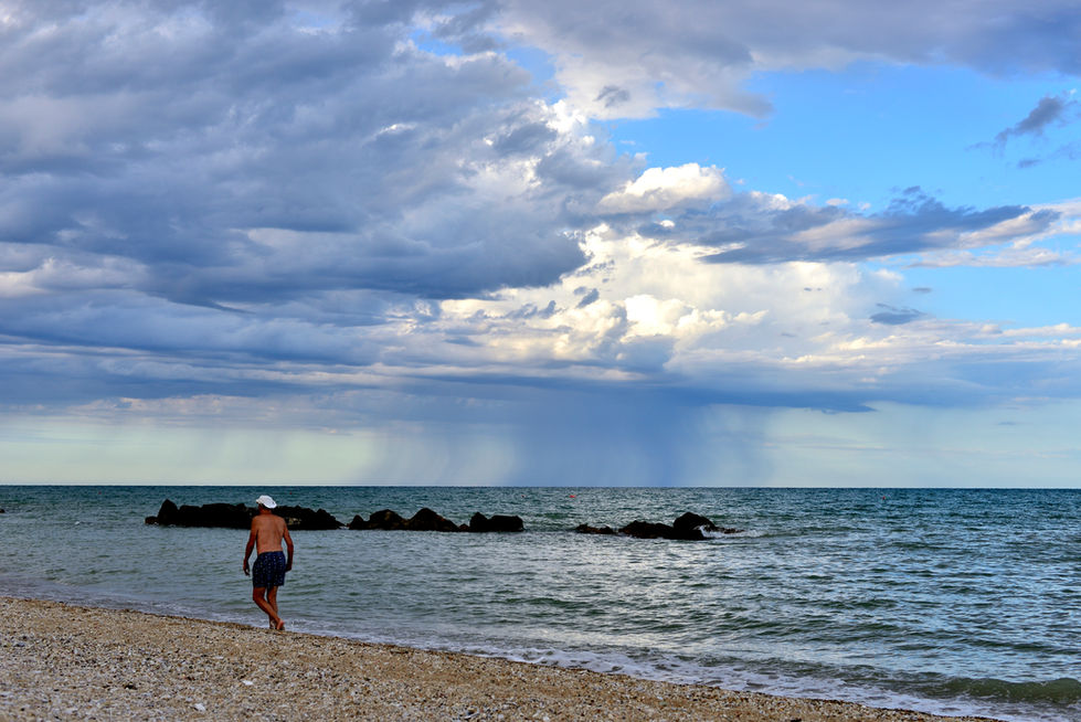Uomo cammina sulla spiaggia verso il mare, con alle spalle nuvole e tromba marina.