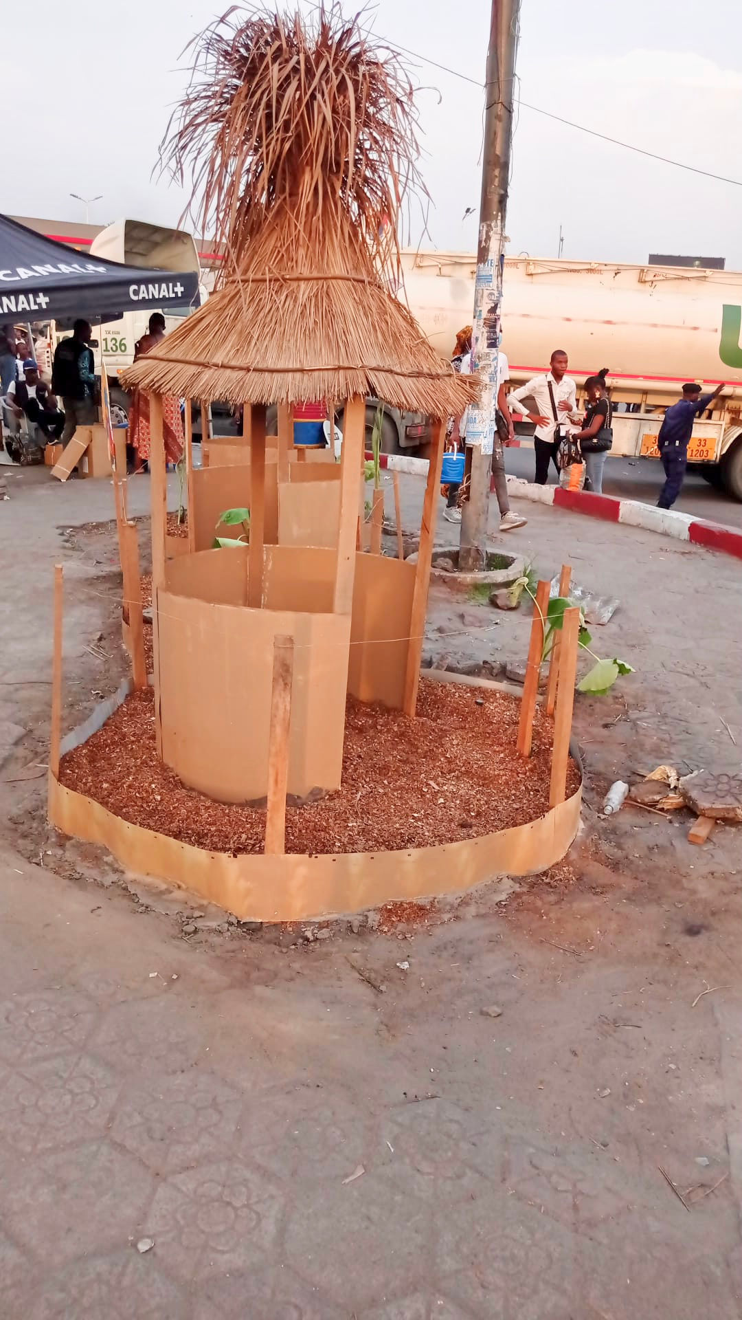 Fabrication d'une haute cabane en tôle, ornée d'un haut toit en paille, représentant une décoration artisanale, rurale et authentique dans une rue.