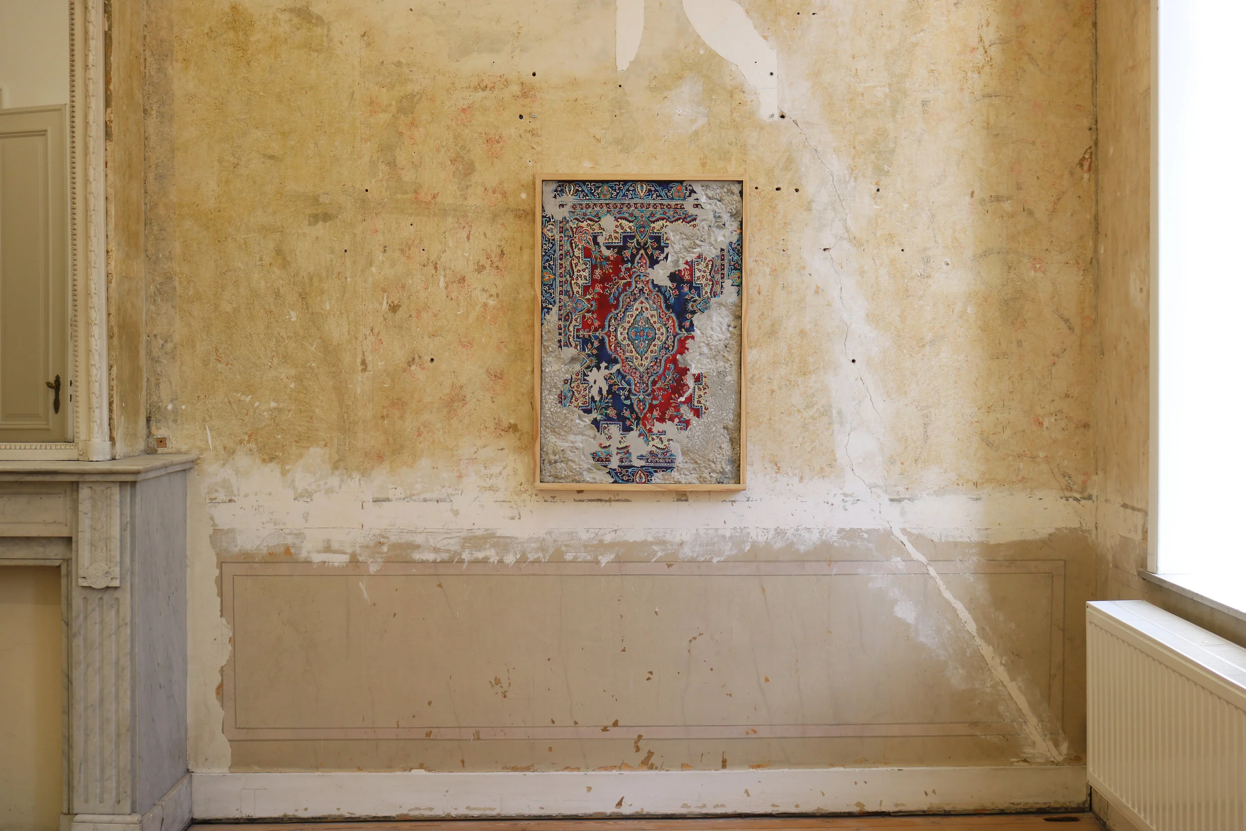 Tapestry artwork by Jason Seife. Framed tapestry with intricate red, blue, and white patterns hangs on a rustic, textured wall, evoking a blend of elegance and vintage charm.