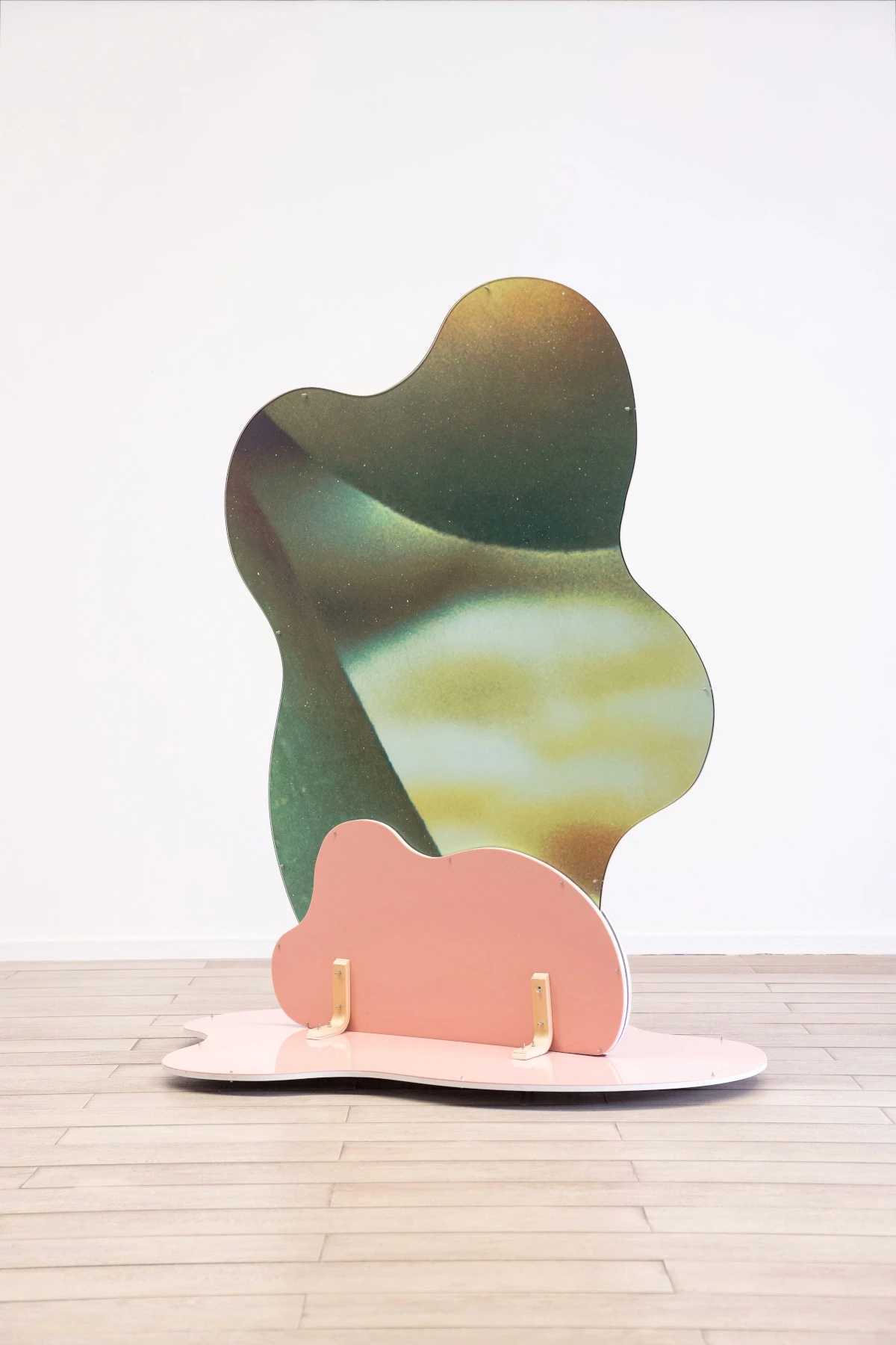 Abstract sculpture with an organic shape and a smooth color gradient of green and yellow. It stands on a pink, wavy base, creating a serene tone. Made by Sara Naim