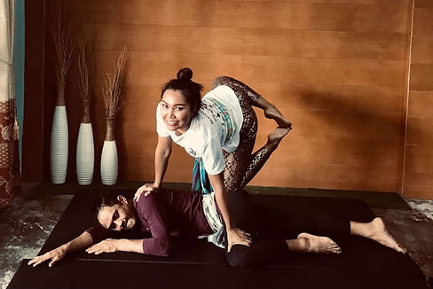 A Thai Warrior Massage session in progress at Jasmine Thai Therapy in Manchester, showcasing a therapist performing a stretching technique on a client, with traditional Thai décor and informational posters in the background, highlighting the cultural and therapeutic services offered.