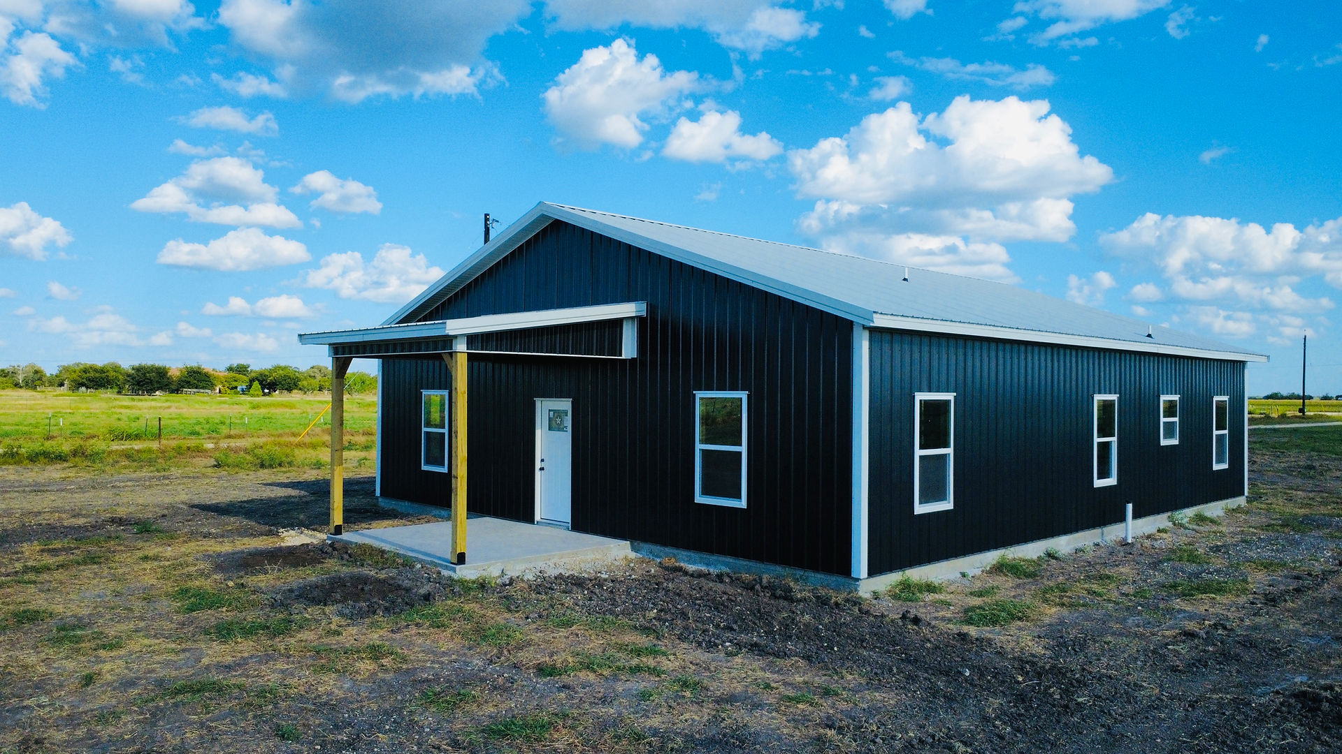 Completed black metal barndominium with white trim, metal roof, and covered front porch.
