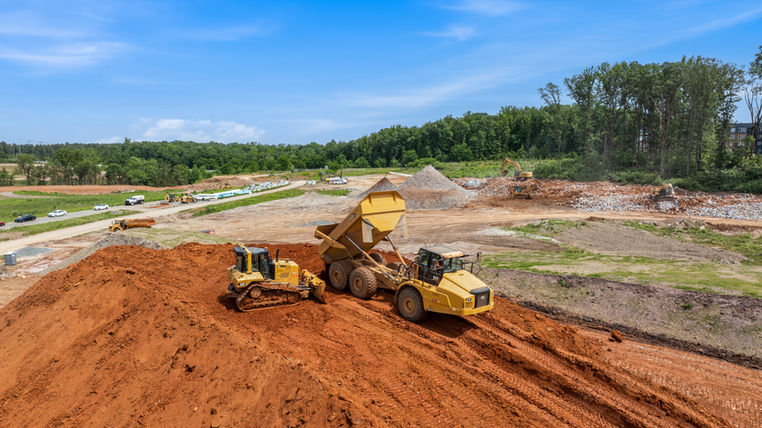 Close-up drone photography captures an aerial view of a construction site actively being cleared by heavy machinery. The image reveals groundwork activities from above, showcasing the early stages of development where the land is prepared for building. Construction equipment is visible in operation, methodically clearing debris and leveling the ground to create a stable foundation. This perspective highlights the scale and precision involved in site preparation, emphasizing both the technology used and the organized effort behind construction projects. Such aerial views are invaluable for monitoring progress and ensuring that groundwork proceeds according to plan, laying the essential groundwork for future construction phases.
