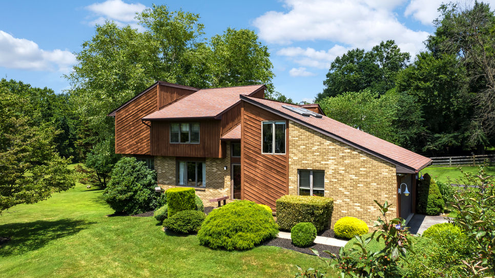 Drone aerial photograph showcasing a striking Mid-Century Modern home surrounded by lush landscaping, featuring clean lines, large windows, and an expansive flat roof under a clear sky. The image captures the architectural design’s integration with its natural environment, highlighting the spacious outdoor areas and geometric shapes characteristic of the style.