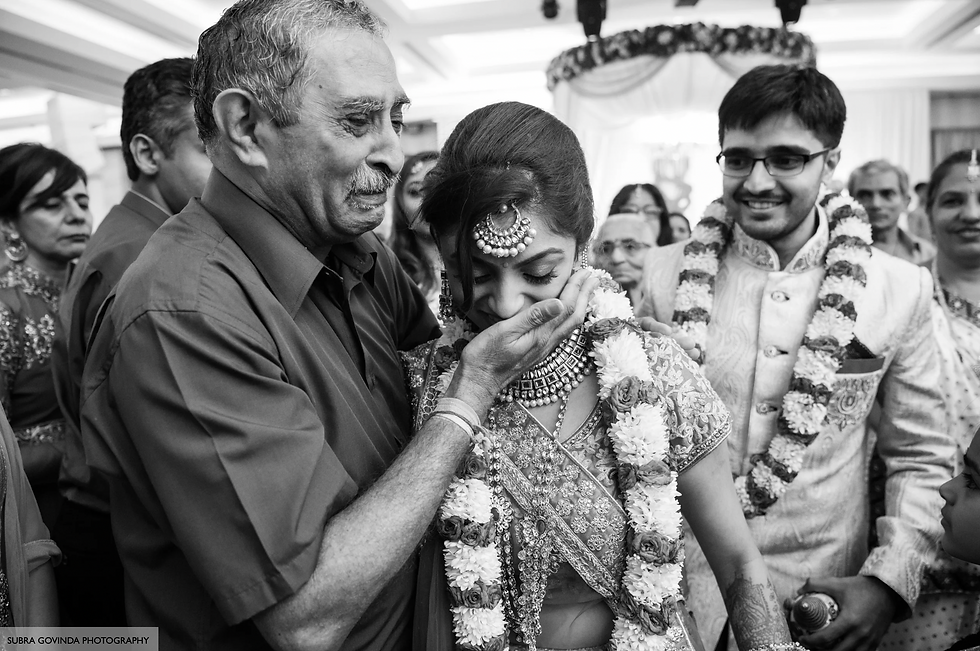 Elderly man tenderly holds adorned woman's face at a wedding, surrounded by smiling guests in decorated hall. Emotional and joyful scene.