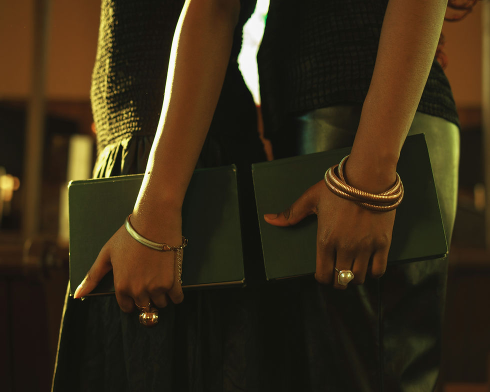 Two people stand side by side holding green books. They wear dark clothing and bracelets. Warm lighting creates a cozy atmosphere.