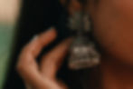 Close-up of a hand adjusting ornate silver earrings with intricate design and small dangling beads. Warm lighting highlights details.
