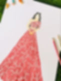Drawing of a woman in a pink floral dress on white paper, surrounded by colored pencils and miniature figures, on a grass background.