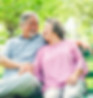 An elderly couple sits on a park bench, smiling together.