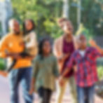 A smiling family of five walks together in a sunny park.