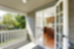 Open French doors reveal kitchen, balcony with white railing, and exterior view.