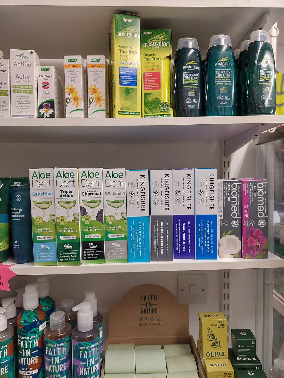 Photo of natural toothpaste and body care products on shelves in a herb shop, portrait, mix of green and colorful packaging, focus on middle shelf with toothpaste boxes
