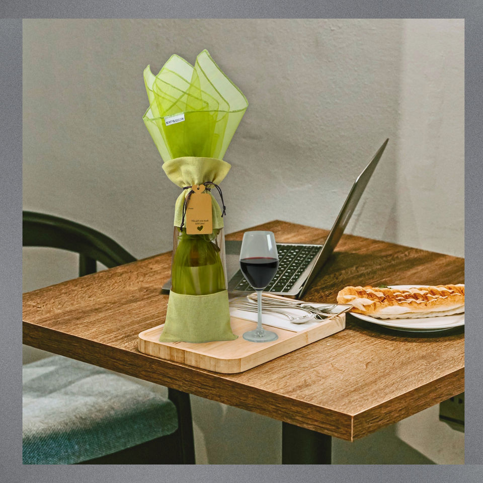 Cotton linen wine bag with moss green organza wrap styled on a dining table beside a laptop, pizza, and a glass of wine.