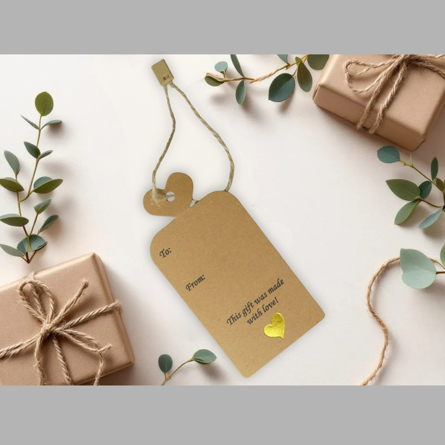 Kraft gift tag with heart-top, To/From, gold-foil heart, and jute snap-lock shown in a neutral flat-lay with wrapped gift box