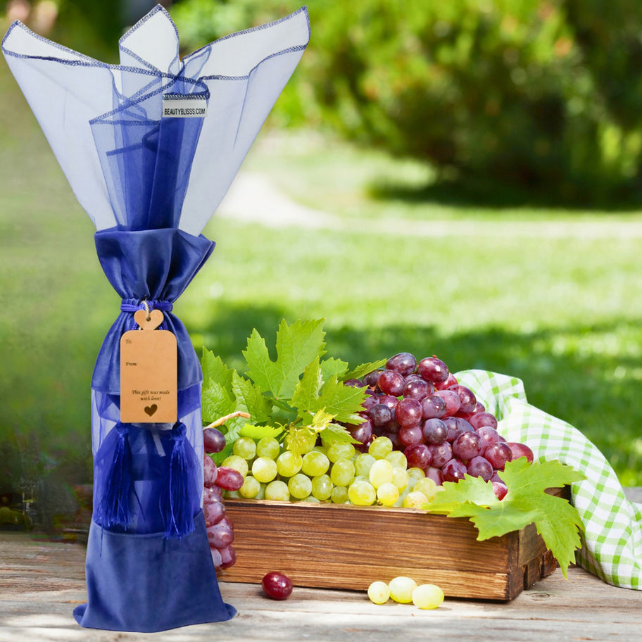 Royal blue velvet wine gift bag styled outdoors beside grapes and greenery in a fresh gift ready lifestyle scene.