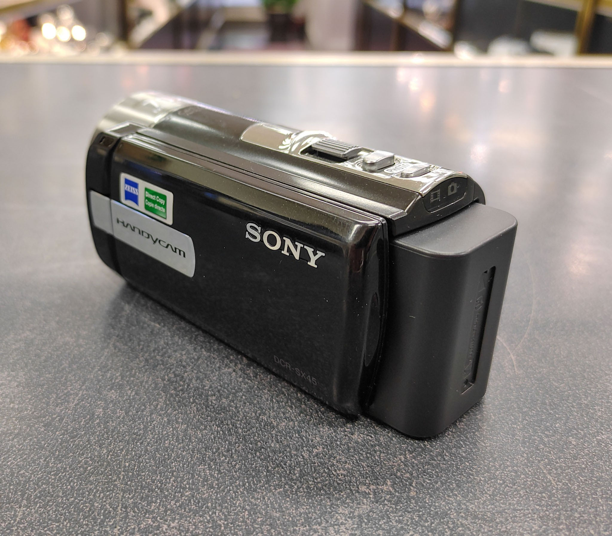 Sony Handycam DCR-SX45 black camcorder shown from multiple angles with flip-out LCD, Carl Zeiss lens, battery compartment