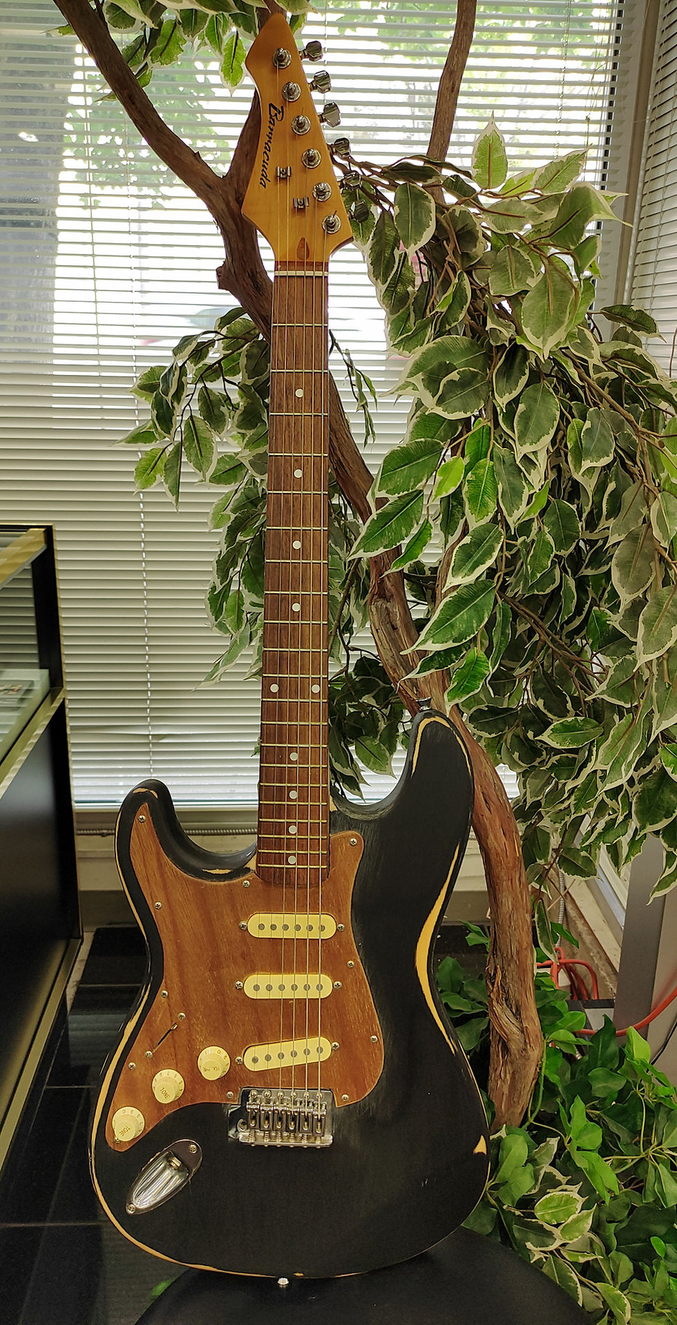 Custom-built left-handed black Barracuda Strat-style guitar with wood pickguard; visible neck-pocket repair and no tremolo