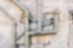 iron-sewer-pipes-on-stone-wall-background-2022-11-15-07-57-43-utc-scaled.jpg