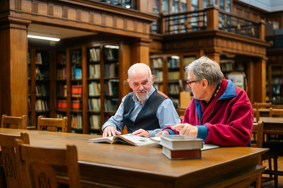 Two people reading and discussing open books together in a library.