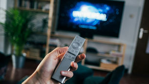 A living room with a tv and a remote in a person's hand.