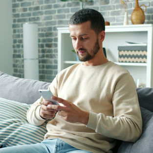 A man relaxing on a sofa while looking at his smartphone.