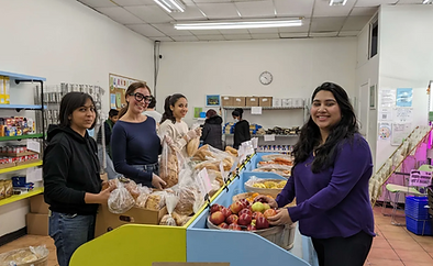 Young women standing in the food bank and smiling as they bag bread and apples