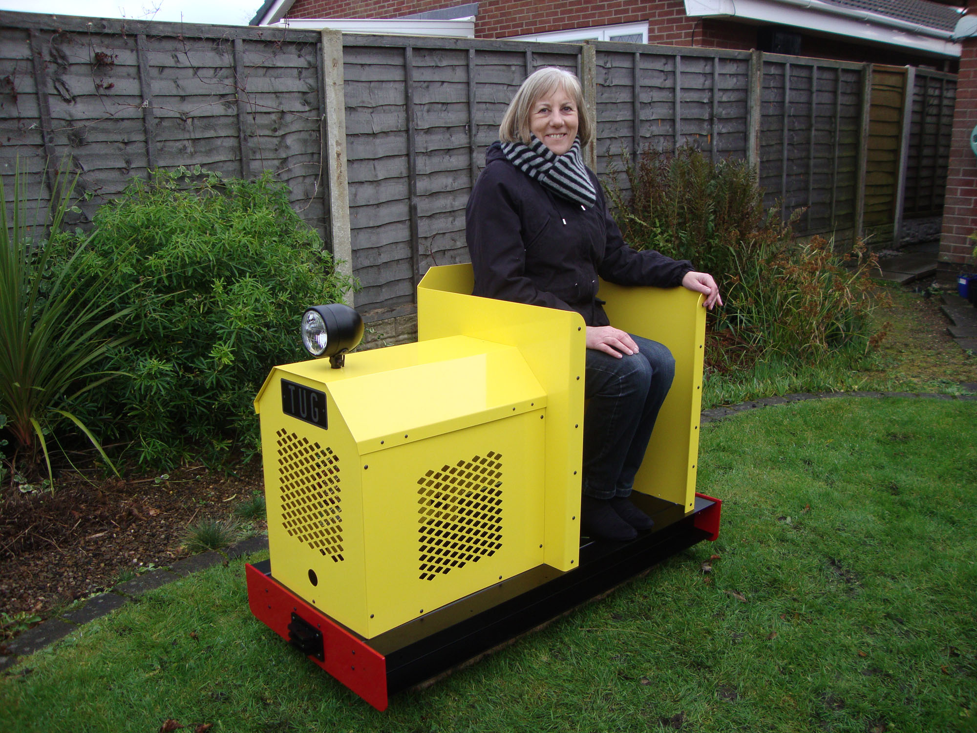 Yellow Phoenix Tug miniature locomotive carrying a passenger on garden railway track