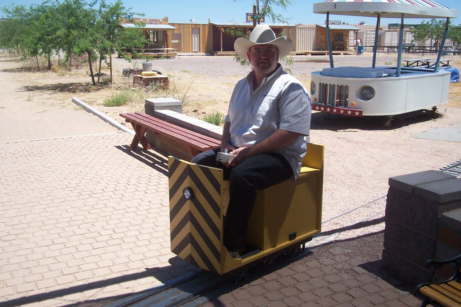 Person in a large white ten-gallon hat operating a yellow industrial miniature locomotive, seen from the front
