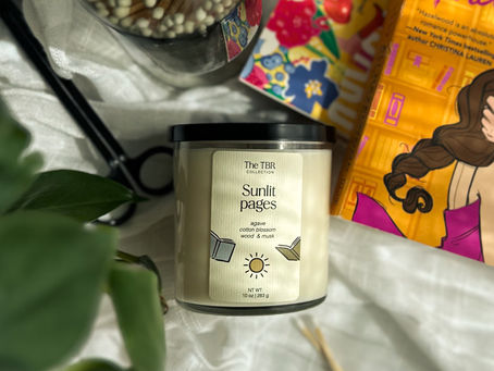 10oz Sunlit Pages candle surrounded by stacked books, wick trimmer, match cloche, and matches