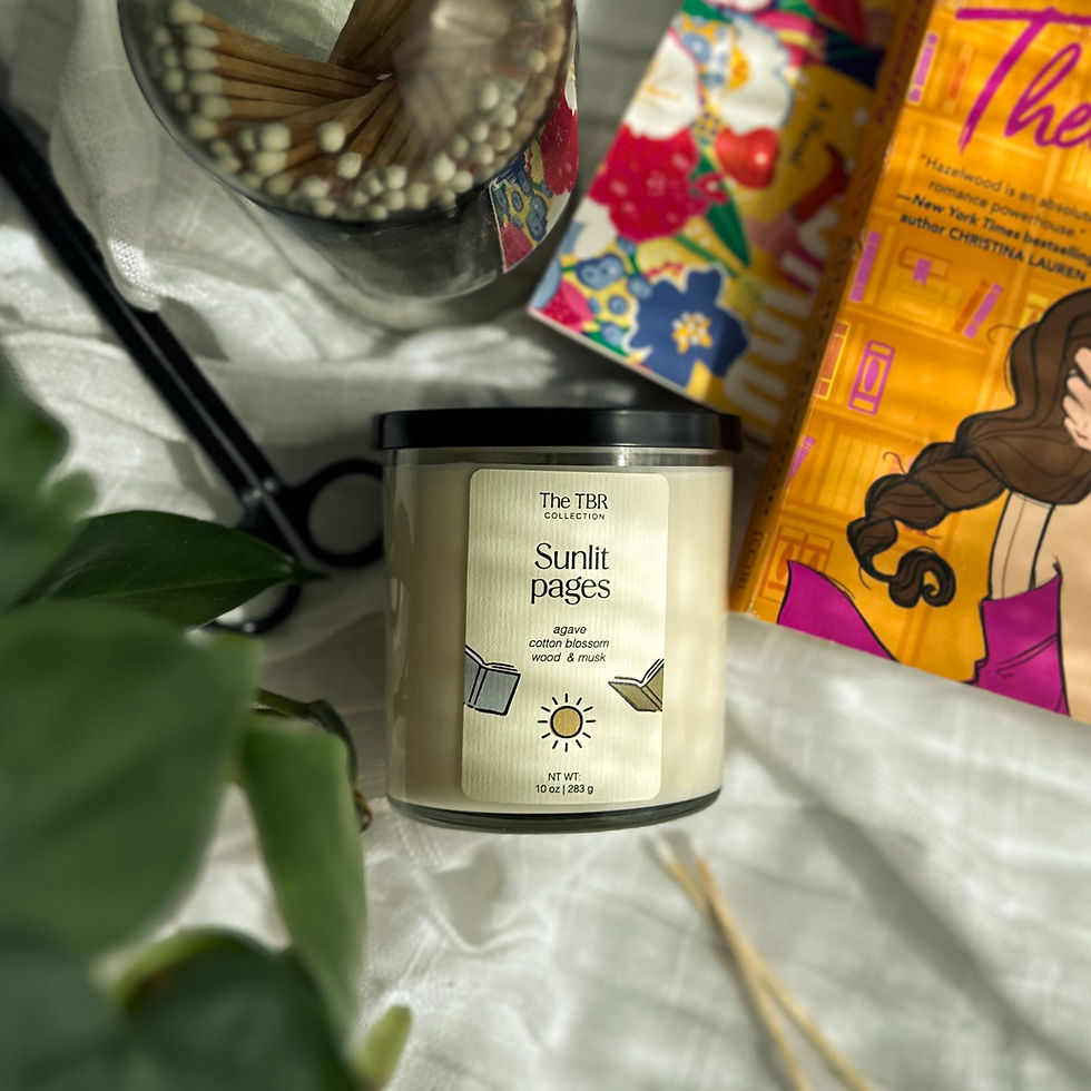 10oz Sunlit Pages candle with dappled sunlight over top, greenery in corner, matches and wick trimmer, accompanied by a stack of romance books.