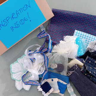 A cardboard box labelled 'Inspiration Inside' next to a collection of blue and white fabric, thread and other sewing embellishments