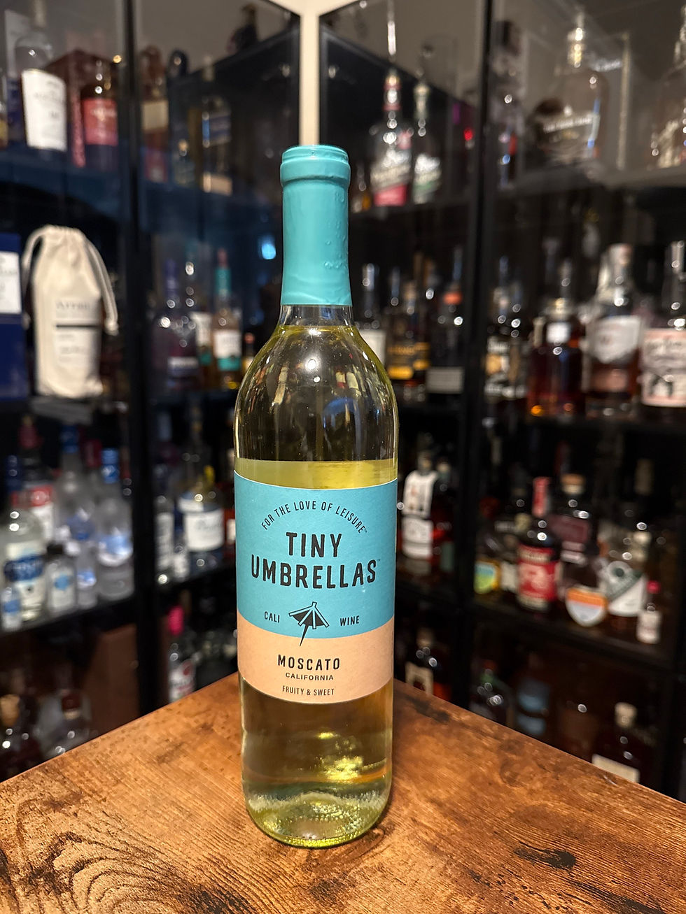 Bottle of Tiny Umbrellas Moscato on a wooden table, with a turquoise label in front of a blurred liquor cabinet.